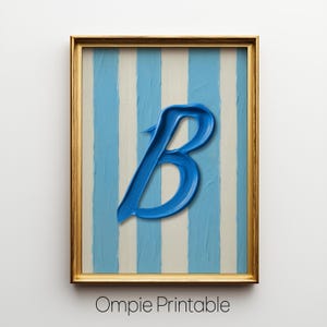 Może przedstawiać: Oprawiona grafika z niebieską namalowaną literą "B" na pasiastym tle w kolorze jasnoniebieskim i złamanej bieli. Złota rama otacza grafikę. Tekst "Ompie Printable" znajduje się na dole.