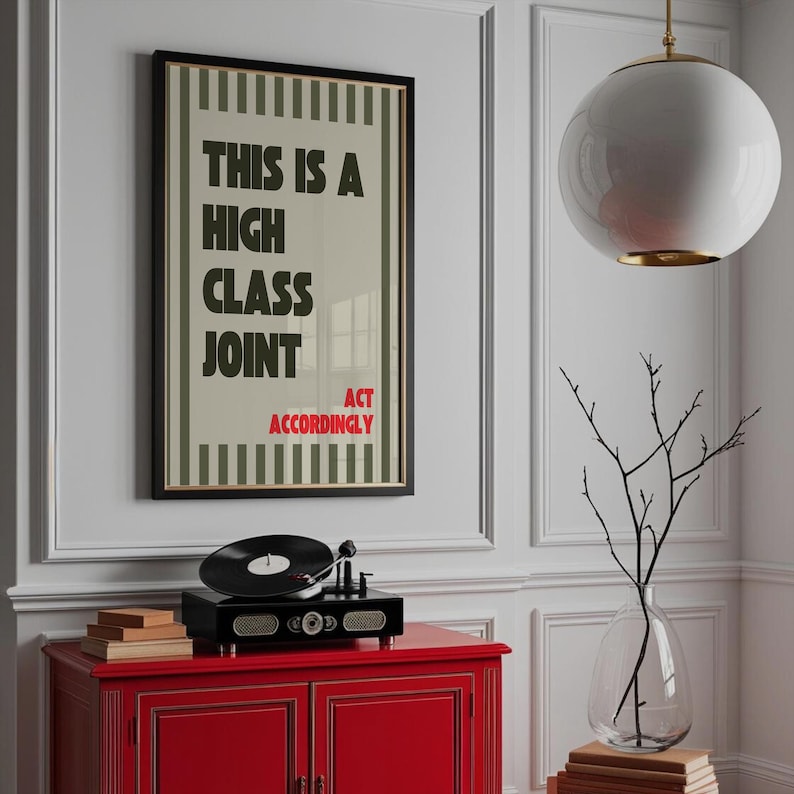 May include: A framed poster with the text "THIS IS A HIGH CLASS JOINT ACT ACCORDINGLY" hangs above a red cabinet. A black record player sits on the cabinet. A white globe light and a glass vase with branches are also in the image.