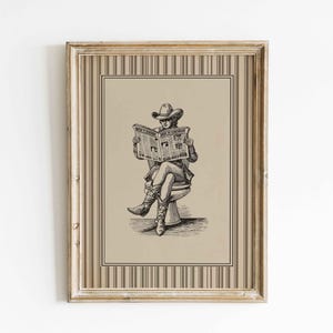 May include: Framed black and white illustration of a person in a cowboy hat and boots reading a newspaper while seated on a toilet. The artwork is in a vintage style, framed in a gold-colored frame with a striped border.