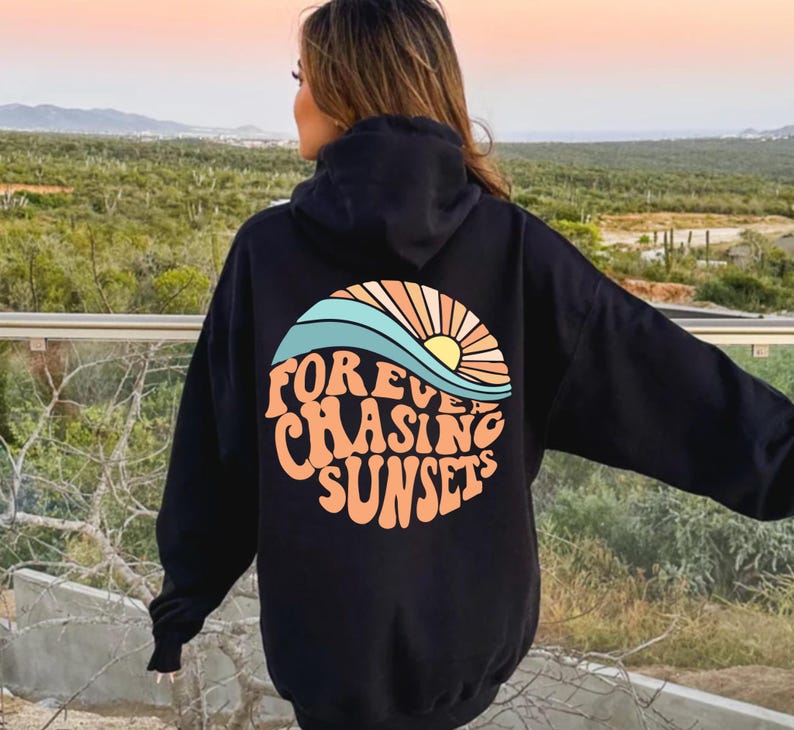 May include: Black hoodie with a colorful graphic on the back. The graphic features a stylized sunset with the words "Forever Chasing Sunsets" in a retro font. The hoodie has a hood and long sleeves.