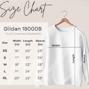 May include: A white Gildan 18000B youth crewneck sweatshirt hangs on a wooden hanger. The image includes a size chart with measurements in inches for width, length, and sleeve length, ranging from XS to XL.