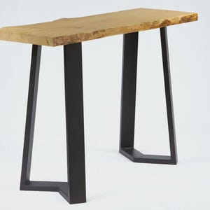 May include: A modern console table with a natural wood top and black metal legs. The tabletop has a live edge, and the legs are a geometric design. The table is approximately 48 inches long.