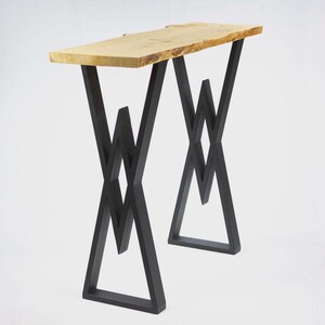 May include: A modern console table with a natural wood top and black metal geometric legs. The tabletop is approximately 48 inches long and has a live edge. The legs are a striking, angular design.