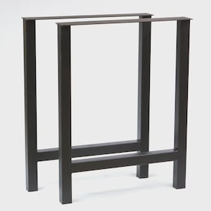 May include: Two dark gray metal table legs. Each leg is rectangular with a horizontal support bar near the bottom. The legs are designed for a modern, minimalist aesthetic. The legs are made of steel.