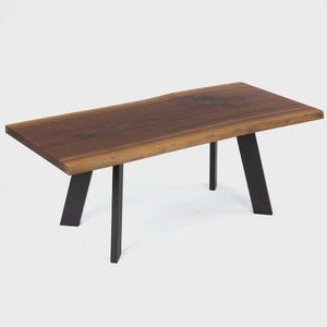 May include: A rectangular coffee table with a live edge wooden top and black metal legs. The tabletop is a rich brown color with natural wood grain. The legs are angled and provide a modern, minimalist aesthetic.