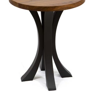 Pode incluir: Mesa redonda pequena com tampo de madeira escura e base de metal preto. O tampo tem aproximadamente 61 cm de di&acirc;metro. A base apresenta um design curvo &uacute;nico com tr&ecirc;s pernas.