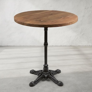 May include: A round wooden table with a dark brown finish. The table has a black metal base with a decorative, ornate design. The table is approximately 30 inches in diameter and stands about 30 inches tall.