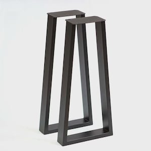 May include: Two black metal table legs. Each leg has a rectangular top and a U-shaped base, with straight, angled supports. The legs are made of a dark, matte metal and are designed for furniture construction.