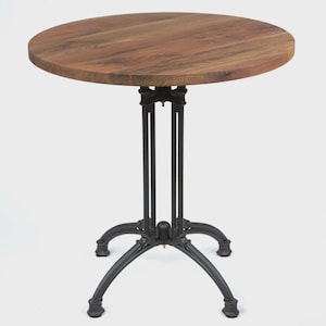 May include: A round wooden table with a dark brown tabletop and a black metal base. The tabletop is made of wood and has a natural grain pattern. The base has a decorative design with curved legs.