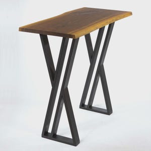 May include: A modern console table with a live edge wood top and black metal legs. The tabletop is a warm brown color, and the legs have an X-shaped design. The table is approximately 48 inches long.