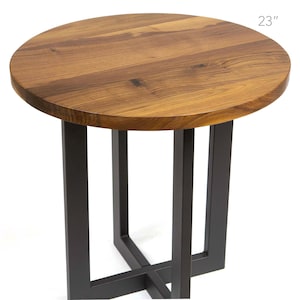 May include: A round wooden side table with a dark brown finish. The tabletop is 23 inches in diameter and rests on a black metal base with a geometric design. The table is suitable for a living room or bedroom.