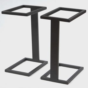 May include: Two black metal side table frames. Each frame has a square top, a rectangular center support, and a square base. The frames are made of a dark, matte metal.