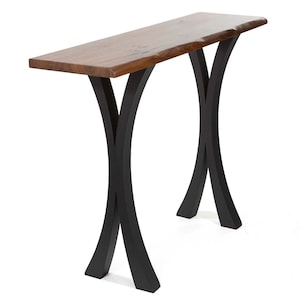 May include: A modern console table with a live edge wooden top and black metal legs. The tabletop is a warm brown color, and the legs are curved, creating an X-shaped design. The table is approximately 48 inches long.
