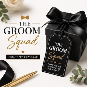 Puede incluir: Una caja de regalo negra con un lazo de satén negro y una etiqueta rectangular negra con texto en blanco y dorado que dice THE GROOM Squad y THANK YOU FOR BEING PART OF OUR BIG DAY. Un bolígrafo dorado descansa sobre una superficie blanca.
