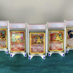 Peut inclure: Cinq cartes à collectionner représentant des personnages Dracaufeu, chacune insérée dans un étui de protection en plastique transparent avec un support blanc. Les cartes présentent diverses illustrations du créature de feu aux tons rouge, orange et jaune.