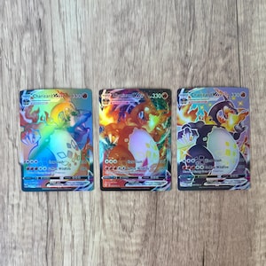 May include: Three Charizard VMAX trading cards. Each card features a holographic design with a Charizard illustration, a large egg, and the text "Charizard VMAX 330". The cards have a Claw Slash and G-Max Wildfire attack.