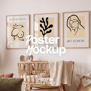 May include: Three framed art prints with botanical and abstract designs hang above a wicker crib. The prints feature black line drawings on a cream background. The crib is filled with a stuffed elephant, a white blanket, and a white sheet.