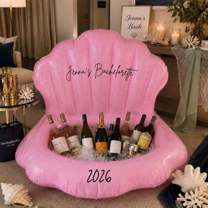 May include: A large, inflatable, light pink seashell-shaped cooler filled with ice and various glass bottles. The text "Jenna's Bachelorette" is printed in black script on the upper shell, and the number "2026" is printed in black on the lower base.