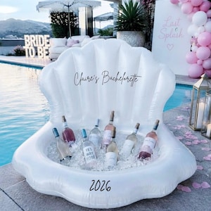 May include: A large, white, inflatable seashell-shaped cooler filled with ice and several glass wine bottles. The text "Claire's Bachelorette" is printed in black script on the upper shell, and the number "2026" is printed in black at the base.