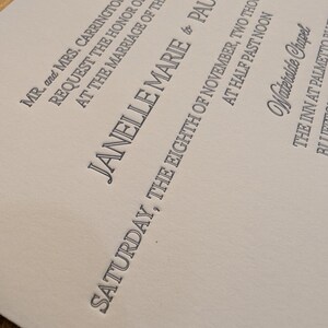 May include: A formal invitation with elegant typography. The text includes names, a wedding date, and the venue, Waterside Chapel. The invitation is printed in dark gray ink on a light beige paper.