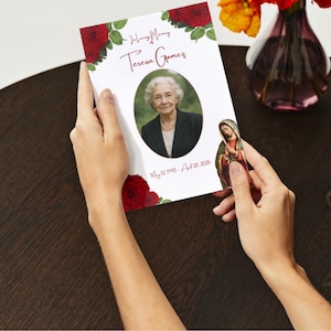 May include: A memorial card with a portrait of a woman, surrounded by red roses and green leaves. The card includes the name "Teresa Gomes" and dates. A small religious icon is held nearby.