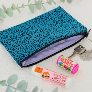Op de afbeelding: Een turquoise etui met luipaardprint en een zwarte ritssluiting, open om een ​​lavendelkleurig interieur te onthullen. Daarnaast liggen sleutels met een "Rhythm is a Dancer" sleutelhanger, een Love Hearts snoeprol en een Malibu Lipcare watermeloen lippenbalsem.