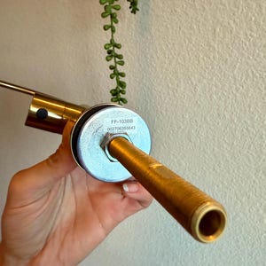 May include: A brass-colored faucet spout with a cylindrical design. The spout has a textured surface and a circular opening. The faucet has a silver-colored base with the text "FF-103BB" and "002706355643".