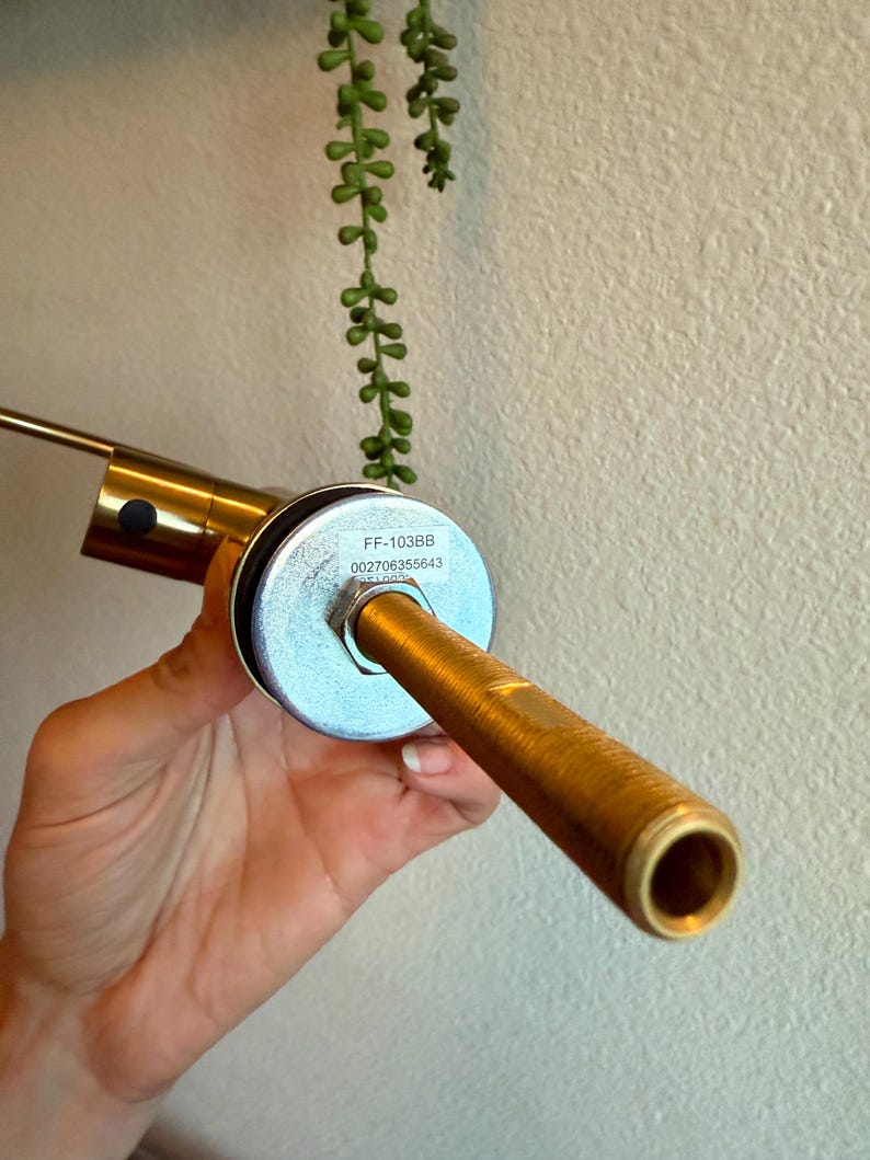 May include: A brass-colored faucet spout with a cylindrical design. The spout has a textured surface and a circular opening. The faucet has a silver-colored base with the text "FF-103BB" and "002706355643".