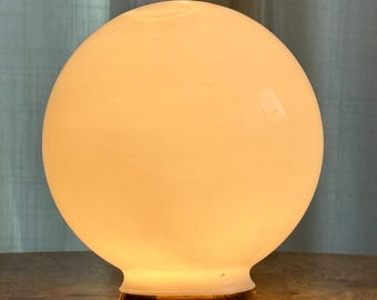 May include: A spherical white glass lamp shade with a smooth, glowing surface. The globe features a circular opening at the bottom, which is securely seated on a dark brown, octagonal wooden base. The light emits a soft, warm, diffused glow.