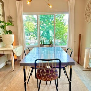May include: A rectangular dining table with a textured gray top and black metal legs, surrounded by four chairs featuring black metal frames, gold-toned wire backrests, and patterned fabric seats, positioned under a brass sputnik chandelier.