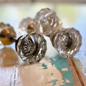 May include: Three clear glass door knobs with an octagonal, faceted design. Each knob features a reflective, multi-sided surface that catches light, attached to a metallic base, showcasing a classic hardware style with a transparent, crystalline appearance.
