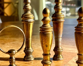 May include: A collection of antique brass lamp finials and a magnifying glass, arranged on a wooden surface. The finials vary in shape, with a gold finish and some showing signs of age. The magnifying glass has a circular lens and a brass handle.