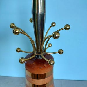 K&ouml;nnte beinhalten: Eine Tischlampe im Mid-Century-Modern-Stil mit einem Messingstiel und dekorativen Armen mit goldenen Kugeln. Der Lampensockel weist abwechselnd braune und goldene B&auml;nder auf. Ein Vintage-Dekorationsartikel.