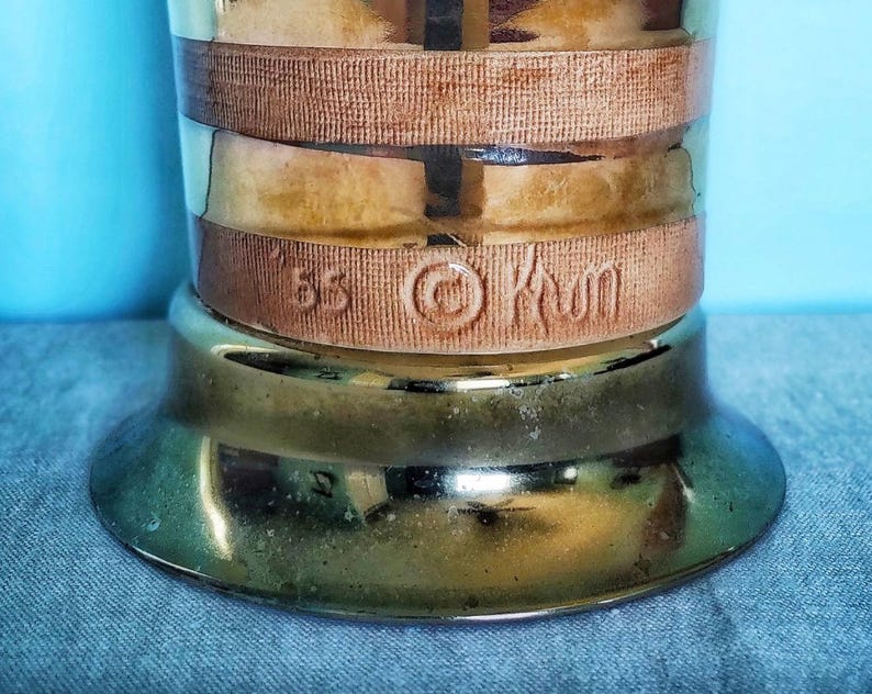 K&ouml;nnte beinhalten: Vintage Troph&auml;enfu&szlig; in Messingfarbe mit breitem, kreisf&ouml;rmigem Fu&szlig; und zylindrischem K&ouml;rper. Der K&ouml;rper hat zwei braune B&auml;nder und ein mittleres Band mit dem gepr&auml;gten Text "85 &copy; Kwm". Der Sockel hat eine gl&auml;nzende, reflektierende Oberfl&auml;che.