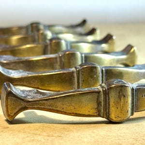 May include: A collection of antique brass drawer pulls, arranged in a row. Each pull has a rectangular center section and curved ends. The brass has a weathered, aged appearance, with visible signs of wear and patina.