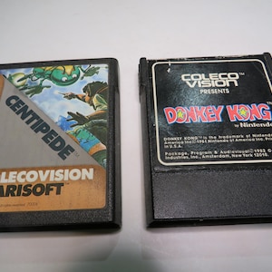 May include: Two vintage ColecoVision video game cartridges. One features the "Centipede" game with a colorful graphic of a centipede and a figure. The other is "Donkey Kong" by Nintendo, with the game title in red and yellow.