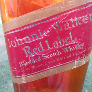 May include: Close-up of a Johnnie Walker Red Label bottle. The red label features gold lettering and a gold border. The text reads "Johnnie Walker Red Label Blended Scotch Whisky".