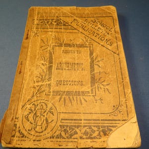 May include: Antique book with a worn, tan cover. The cover features the title "Regents' Arithmetic Questions" in a decorative frame, with the text "School Bulletin Publications" diagonally across the top. The book has a vintage aesthetic.