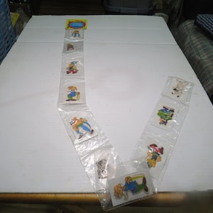 May include: A vertical strip of clear plastic packaging containing ten individual Asterix and Obelix character stickers. Each sticker features a colorful cartoon illustration of characters from the series, arranged in a sequence on a white surface.