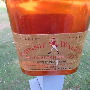 May include: A close-up of a Johnnie Walker bottle. The label features the words "Johnnie Walker Established 1820" and an illustration of a man in a red coat. The bottle is amber-colored and appears to be made of glass.