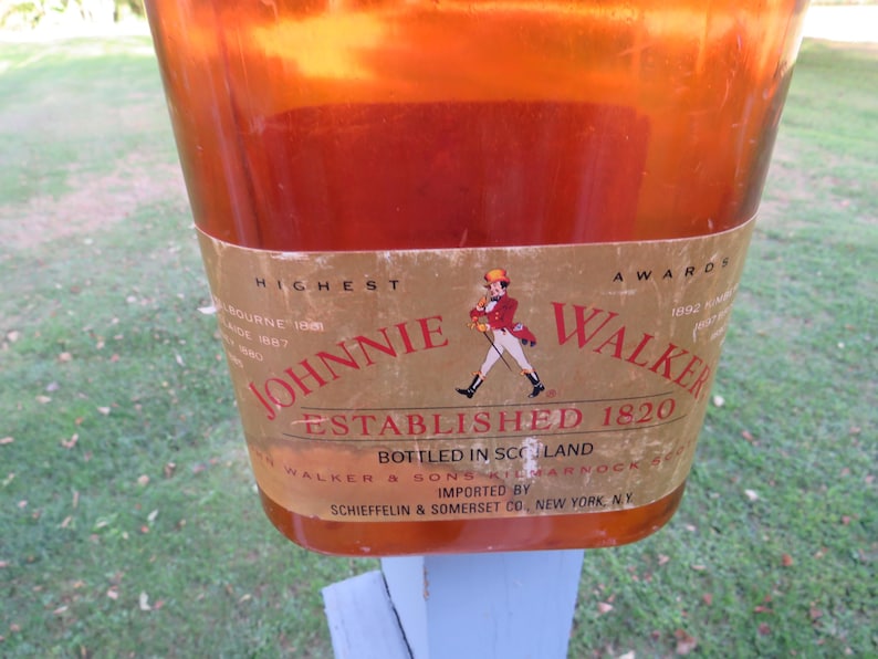 May include: A close-up of a Johnnie Walker bottle. The label features the words "Johnnie Walker Established 1820" and an illustration of a man in a red coat. The bottle is amber-colored and appears to be made of glass.