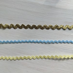 Puede incluir: Tres tipos diferentes de ribete en zigzag. El ribete superior es de purpurina dorada, el ribete del medio es azul claro y el ribete inferior es amarillo p&aacute;lido.