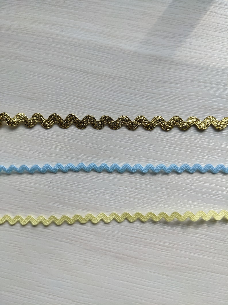 Puede incluir: Tres tipos diferentes de ribete en zigzag. El ribete superior es de purpurina dorada, el ribete del medio es azul claro y el ribete inferior es amarillo p&aacute;lido.