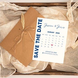 Puede incluir: Una bandeja de madera rústica con un sobre de papel kraft atado con hilo y una tarjeta 'Save the Date'. La tarjeta muestra los nombres 'Jessica & James', un calendario de agosto de 2025 y la fecha del 24 de agosto de 2025. Una ramita de trigo y tela color crema completan el arreglo.
