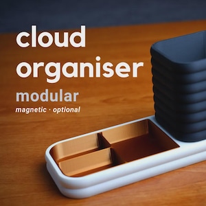 May include: A modular cloud organiser in white, black, and gold. The organiser has a rectangular base with compartments and a tall, ribbed container. Text on the image reads: cloud organiser, modular, magnetic, optional.