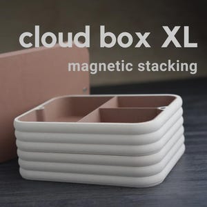 May include: A white and pink cloud box XL with magnetic stacking. The box has a square shape with a lid and is divided into compartments. The lid and interior are pink, while the exterior is white. The text "cloud box XL" and "magnetic stacking" are visible.