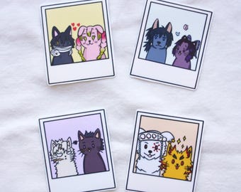 May include: Four square stickers with cartoon animal illustrations in a polaroid style. The stickers feature pairs of cats and dogs in various colors, including black, pink, blue, purple, white, and yellow. Each image has a white border and a colored background.