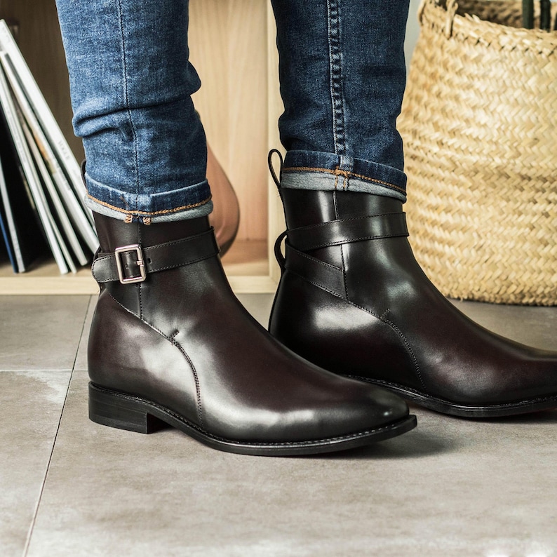 K&ouml;nnte beinhalten: Dunkelbraune Leder-Ankle Boots mit Schnallenriemen. Die Stiefel haben ein elegantes, poliertes Aussehen und werden mit blauen Jeans getragen. Die Stiefel haben einen niedrigen Absatz und eine runde Spitze. H&ouml;he: ca. 25 cm.