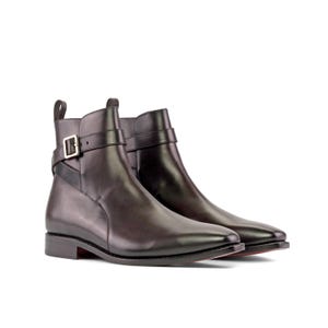 K&ouml;nnte beinhalten: Ein Paar schwarze Leder-Ankle-Boots mit spitzer Zehenpartie. Jeder Stiefel hat einen Riemen mit einer silbernen Schnalle um den Kn&ouml;chel. Die Stiefel haben einen kleinen Absatz und eine Zuglasche hinten. Die Sohlen haben einen roten Akzent.