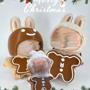 Könnte beinhalten: Zwei Plüsch-Hasenfiguren mit braunen und cremefarbenen Hüten und Lebkuchenmann-Kostümen. Das Bild hat den Text "Merry Christmas" in weißer Schrift mit einem festlichen grün-weißen Rand.